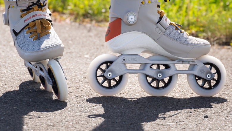 A focused, ground-level shot of a skater wearing grey Powerslide inline skates from the ankles down, standing on a light-colored asphalt path.