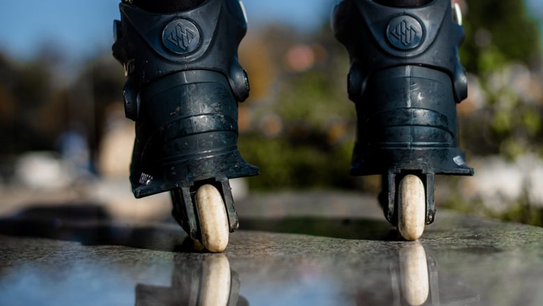 A rear-view, ground-level shot of a skater standing on a smooth, reflective surface in black aggressive inline skates.
