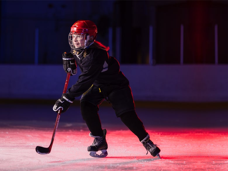 Women's hockey player putting on women's hockey shoulder pads