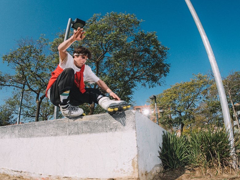 Person performing an inline skate trick on a concrete ledge against a background of trees and a blue sky.