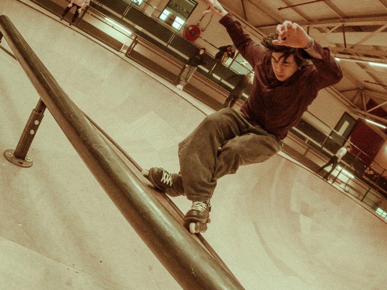 An aggressive inline skater grinding on a rail at an indoor skate park